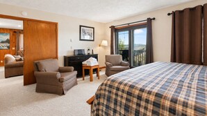 Habitación de hotel con cama, dos sillones, un escritorio, una lámpara y vistas al exterior.