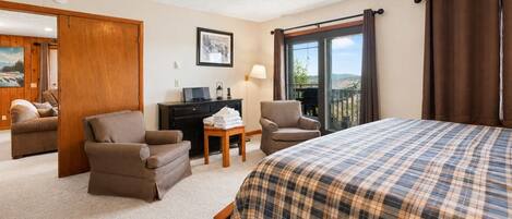 Habitación de hotel con cama, dos sillones, un escritorio, una lámpara y vistas al exterior.