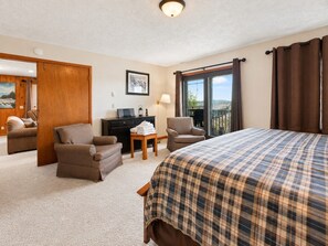 A hotel room with a bed, two armchairs, a desk, a lamp, and a view of the outdoors.