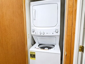 Un appareil combiné lave-linge et sèche-linge à chargement frontal, de couleur blanche, doté d’un panneau de commande, d’une porte et d’un cadre de porte en bois.