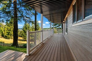 A wooden deck with a railing, a covered porch, and a view of trees and a clear sky.