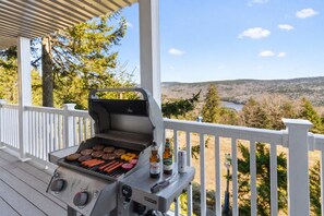 Un barbecue installé sur une terrasse en bois, offrant une vue panoramique sur des collines et un lac.