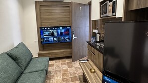 A compact living space with a sofa, a television mounted on a wooden panel, a refrigerator, and a microwave. - 3 Antica jabalal-lwebdeh (Amman)