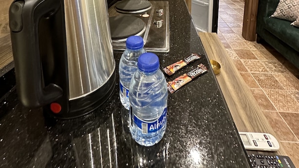 A kitchenette with a coffee maker, water bottles, a scale, and a remote control on the counter. - 3 Antica jabalal-lwebdeh (Amman)