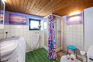 A bathroom with a shower, toilet, sink, and a window with a view of the sky.