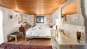 Un dormitorio con techo de madera, una cama con ropa de cama blanca, un tocador, una banca y un espejo grande.