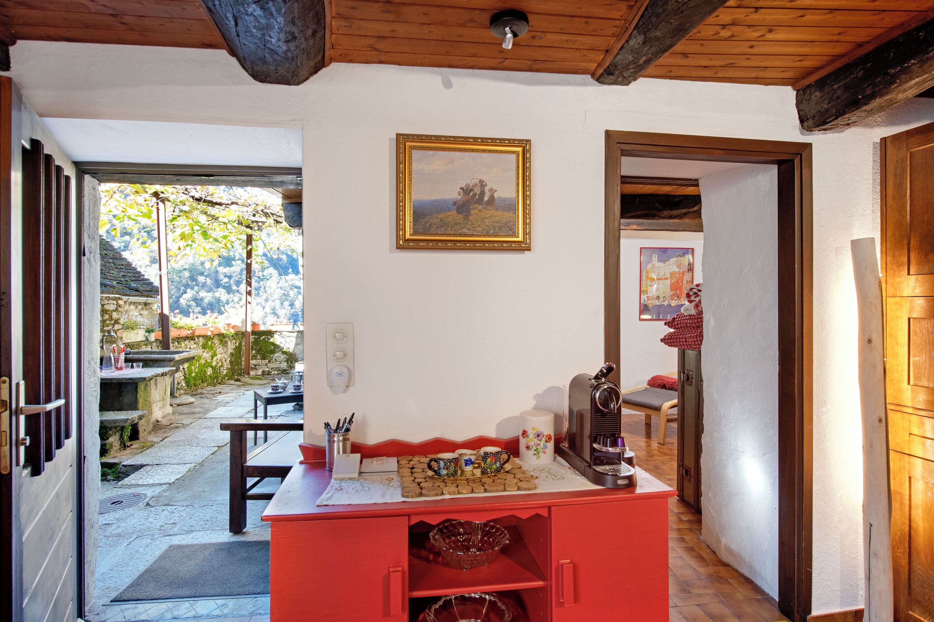 Un intérieur chaleureux avec un plafond en bois, un comptoir rouge orné d’une machine à café et un tableau accroché au mur.
