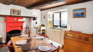 Un comedor con una mesa de madera preparada para cuatro personas, una chimenea roja y vistas al mar a través de una ventana.