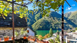 Un edificio de piedra con macetas escalonadas, vista a un lago y un paisaje montañoso.