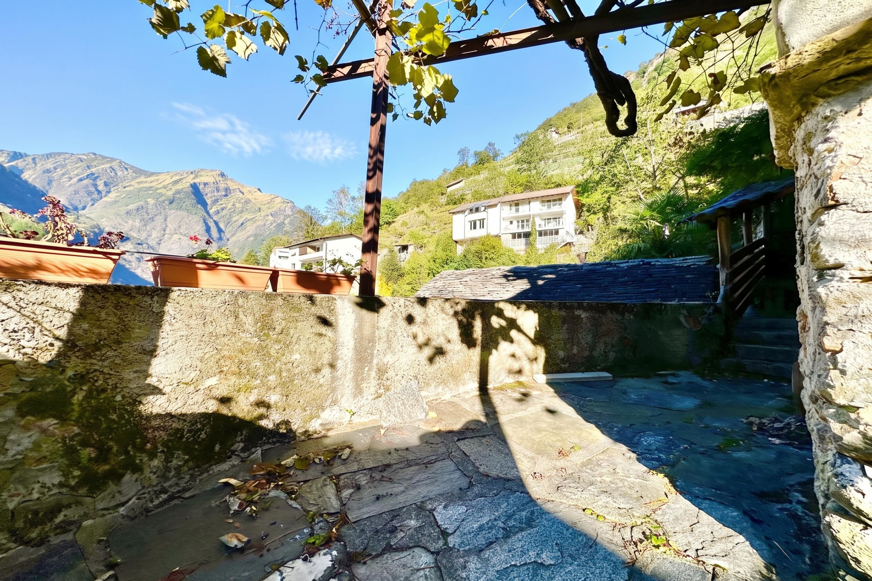 Un patio de piedra con una pérgola, un muro de piedra y vistas a la montaña.