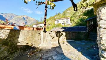 Un patio de piedra con una pérgola, un muro de piedra y vistas a la montaña.