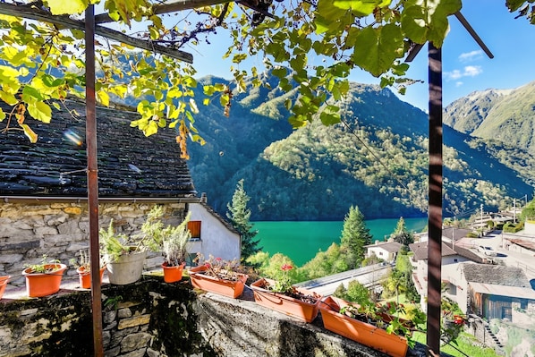 A stone building with terraced potted plants, a clear view of a lake, and surrounding mountains.