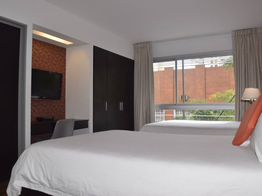 Habitación de hotel con una cama grande, un escritorio con silla, televisor montado en la pared y una ventana con cortinas.