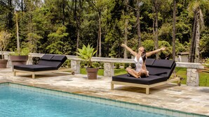 A poolside area with lounge chairs and a potted plant. - Chalés Realli (Bocaina de Minas)