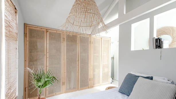 Ein Schlafzimmer mit einem Bett, einer Topfpflanze, einem großen Fenster und einem Kleiderschrank.