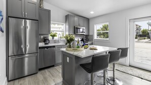 A modern kitchen with stainless steel appliances, a central island with bar stools, and large windows offering a view of the outside.