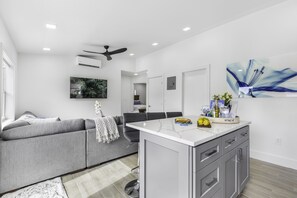 A modern kitchen with a central island, grey sofa, and a dining area.