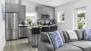 A modern kitchen with grey cabinets, stainless steel appliances, and a grey sofa with patterned cushions.