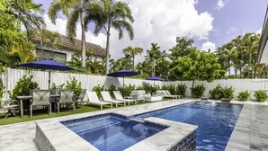 A swimming pool with two sections, surrounded by a white fence, with lounge chairs and umbrellas.