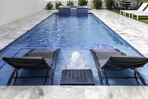 A rectangular swimming pool with a tiled deck and two lounge chairs.
