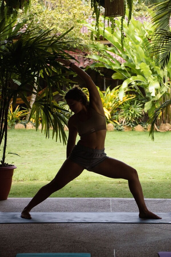 Una persona realizando una postura de yoga sobre una esterilla al aire libre, con abundante vegetación de fondo.