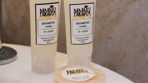 Kaksi pulloa Paradise-shampoota ja yksi palasaippua valkoisella alustalla.