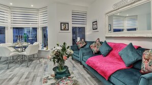 A modern living room with a teal sofa, a dining table with chairs, and a large mirror.
