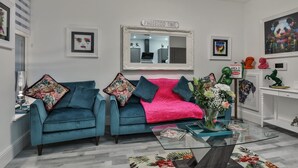 A living room with two teal sofas, a pink throw blanket, a glass coffee table, and a mirror with 'PROSECCO TIME' above it.