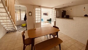 Un comedor con una mesa y sillas de madera, una escalera y una zona de cocina con pared de ladrillo y lámparas colgantes.