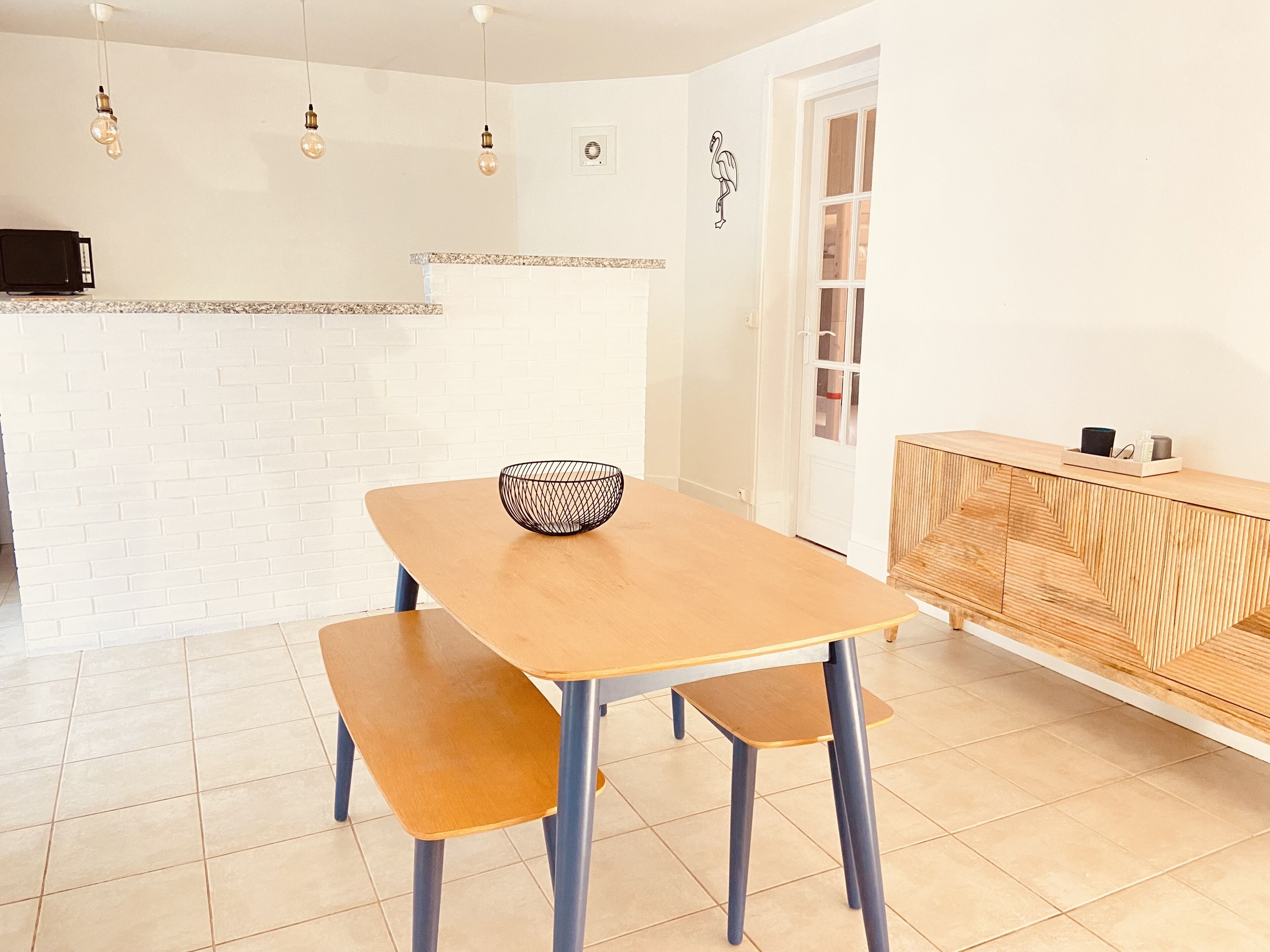 Una cocina moderna con un salpicadero de ladrillo blanco, una mesa de comedor de madera con bancos y un aparador de madera con un diseño geométrico.