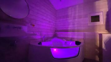 Habitació amb paret de fusta, banyera blanca amb il·luminació morada i una finestra petita, així com una porta blanca.