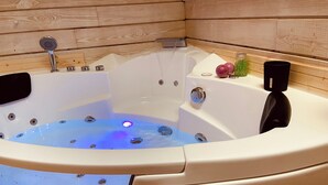 Un jacuzzi con interior de madera, un panel de control y algunos detalles como una botella y una taza.