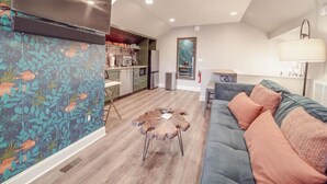 Un salon moderne avec un canapé bleu, une table basse en bois et un coin cuisine à l’arrière-plan.