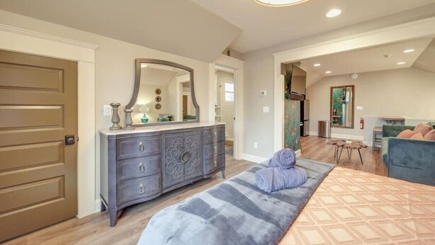 Une chambre à coucher comprenant un lit, une commode, un miroir et un coin salon avec une chaise et une table.