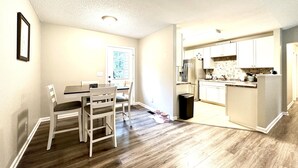 Una cocina moderna con armarios blancos, un refrigerador de acero inoxidable y un comedor con mesa y sillas de madera.