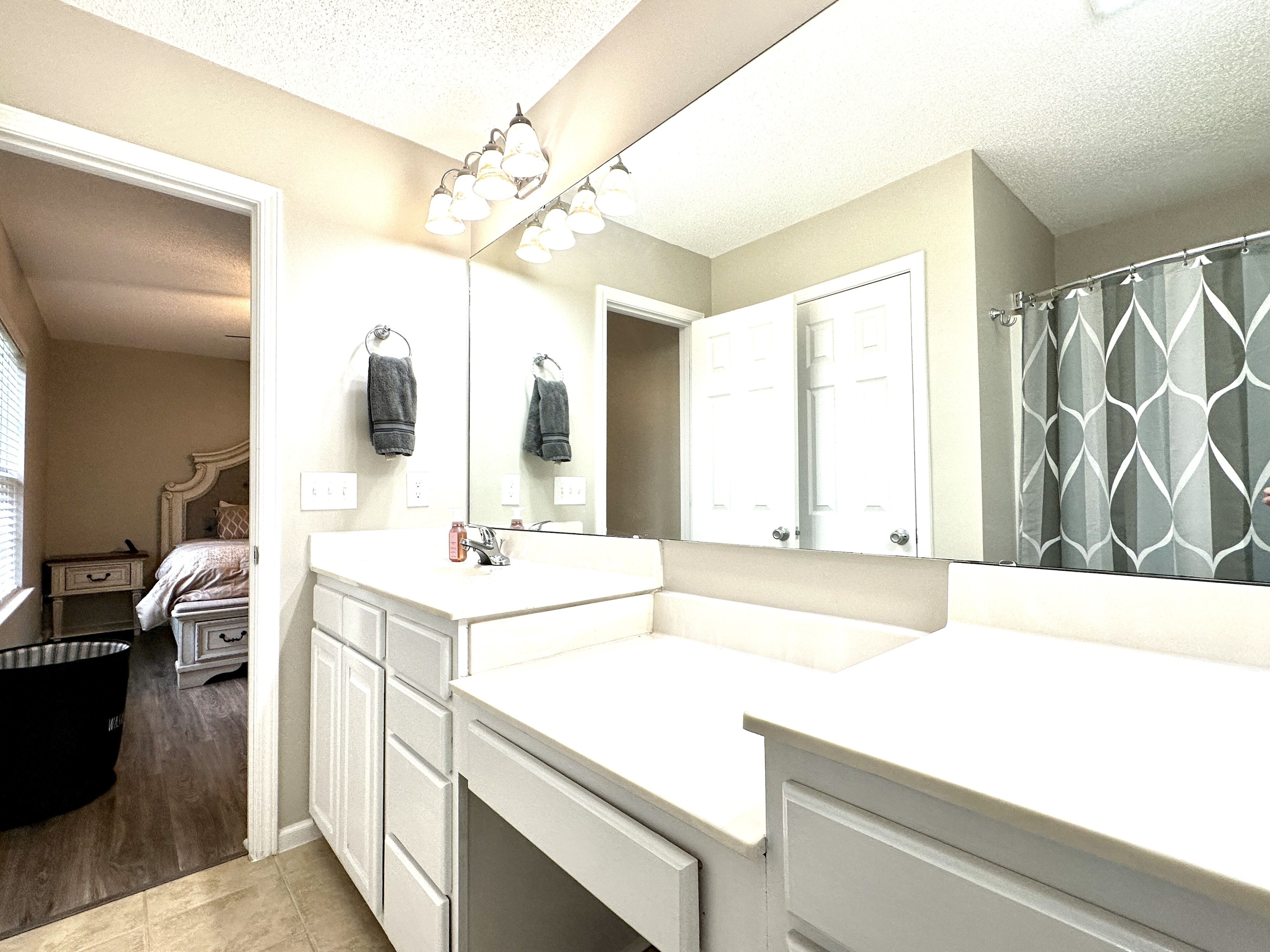 A bathroom with a large mirror, a vanity with a sink, and a shower area.