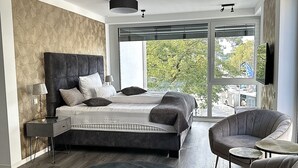 Un dormitorio moderno con una cama grande, un rincón de descanso con una silla y una mesita, y vistas al exterior a través de amplios ventanales.