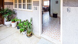 A hallway with a tiled floor, a door leading to a dining area, and potted plants along the wall. - Agradável apartamento no Caiçara (Praia Grande)