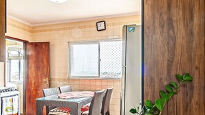 A kitchen with a dining table, chairs, a refrigerator, and a clock on the wall. - Agradável apartamento no Caiçara (Praia Grande)