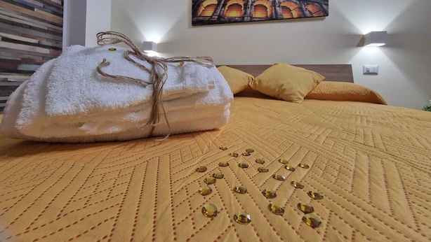 A neatly made bed with a yellow quilt, a decorative pillow, and a white bag tied with a string on a wall with a painting of the Colosseum.