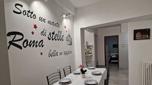A dining area with a table set for four, white walls, and a decorative phrase in Italian.