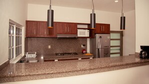 A modern kitchen with granite countertops, wooden cabinets, stainless steel appliances, and pendant lighting. - CASA BENCHITO (Tulum)