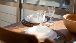 Une table à manger avec des assiettes, des verres et un saladier, placée devant une fenêtre donnant sur la ville.