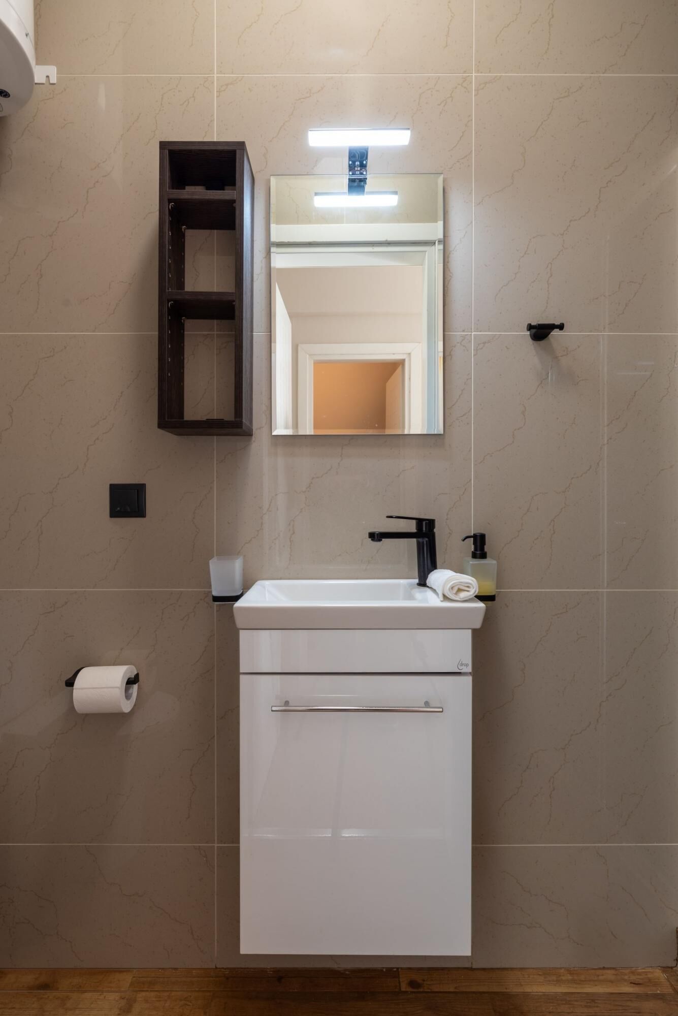 A bathroom with a white sink, a mirror above it, a towel rack, a soap dispenser, and a toilet paper holder.
