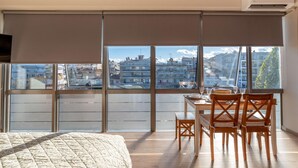 Une chambre avec une grande fenêtre, un lit et un coin repas comprenant des chaises et une table.