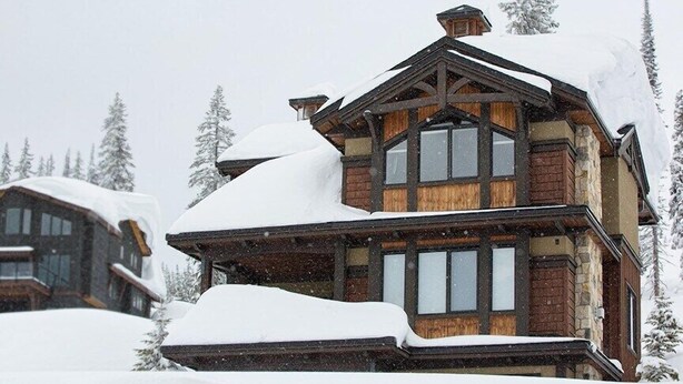 A multi-story log cabin with a snow-covered roof and large windows, surrounded by snow-covered trees. - Dwight Out Chalet w/Hot Tub (Beaverdell)