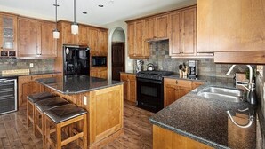 A kitchen with wooden cabinets, granite countertops, a refrigerator, stove, and bar stools. - Dwight Out Chalet w/Hot Tub (Beaverdell)