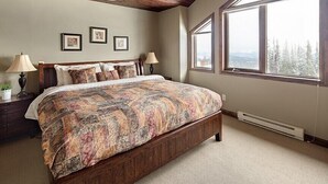 A bedroom with a large bed, wooden headboard, two bedside lamps, a window with a view of trees, and a ceiling with exposed beams. - Dwight Out Chalet w/Hot Tub (Beaverdell)