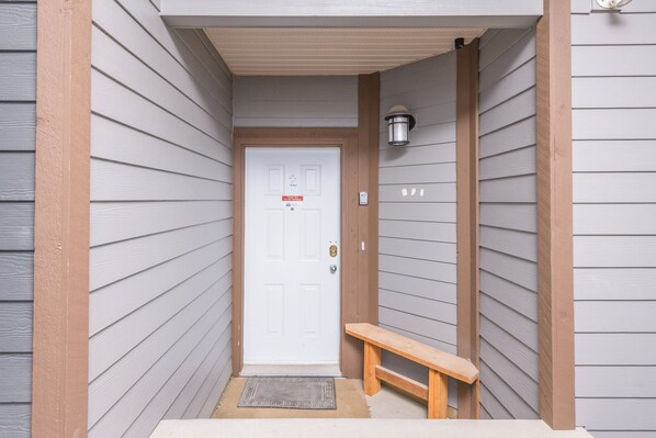 A narrow entrance with a white door, a bench, and a wall-mounted light fixture.