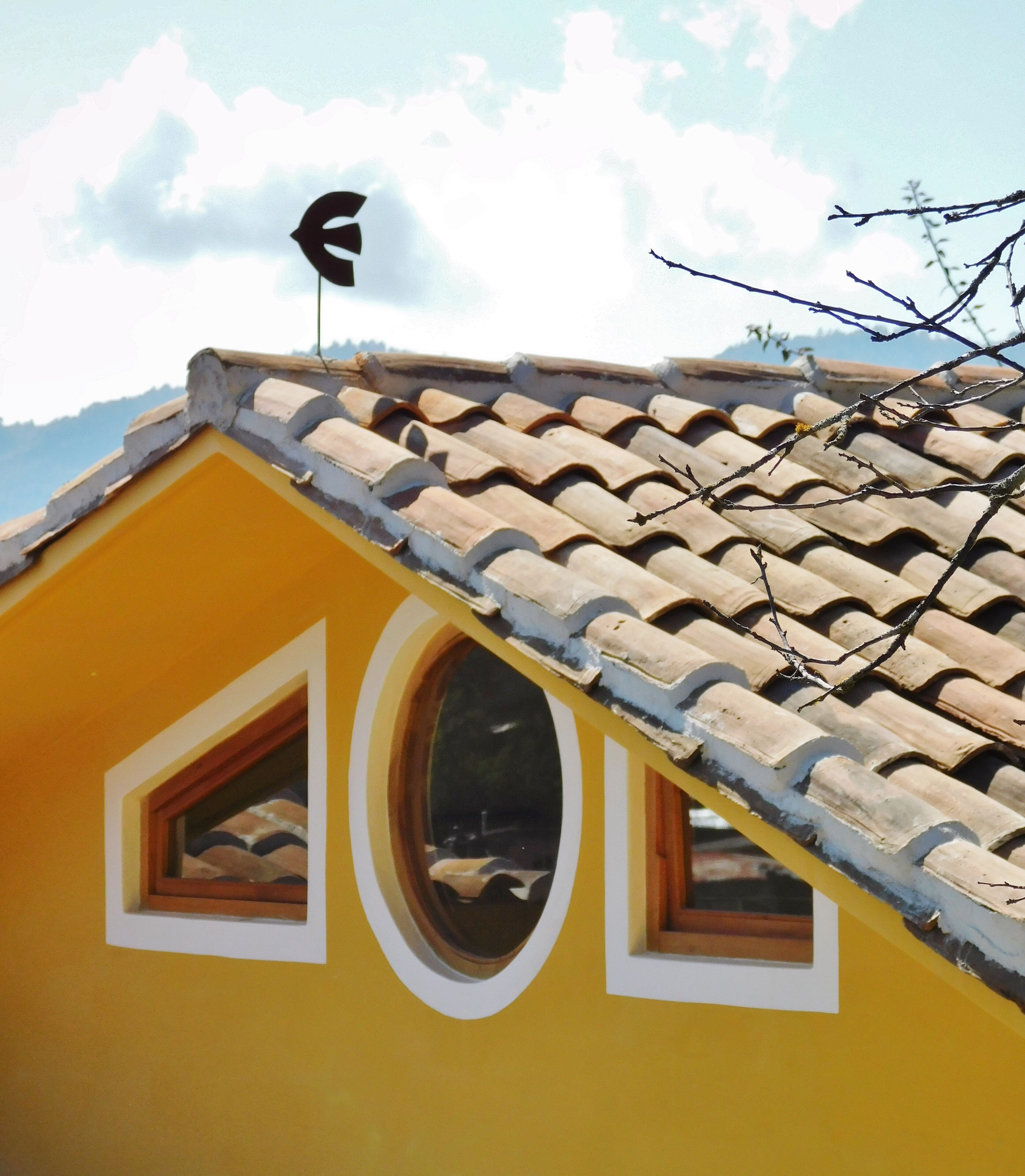 A yellow building with a tiled roof and a small window.
